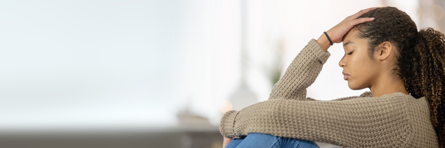 A woman sitting sideways holding her hand on her forehead